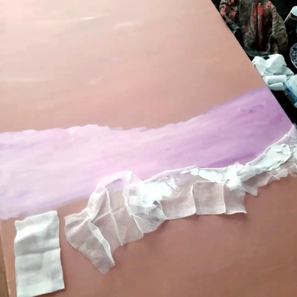 Studio photo: pale strips of gauze bandage laid into still-wet purple paint, on a canvas with a pink ground.