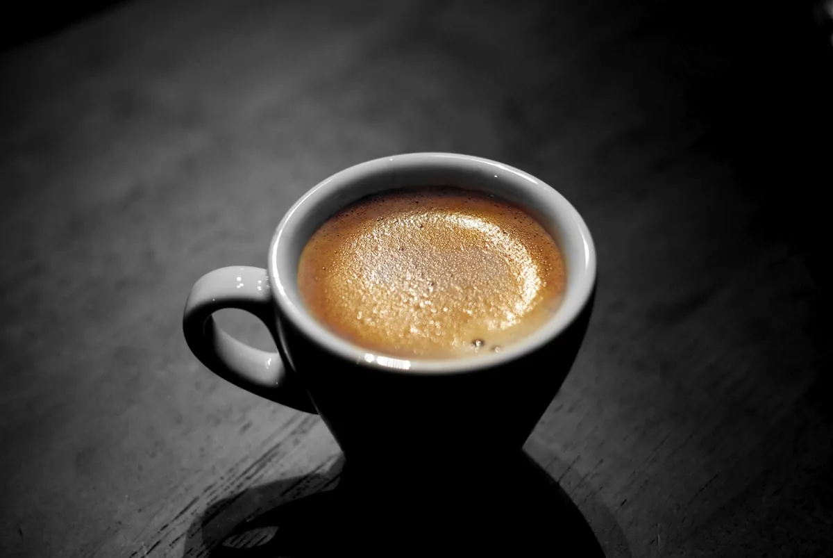 Eine dunkle Espressotasse auf schwarzem Holz, die goldene Crema fängt das einzige Licht im Raum.