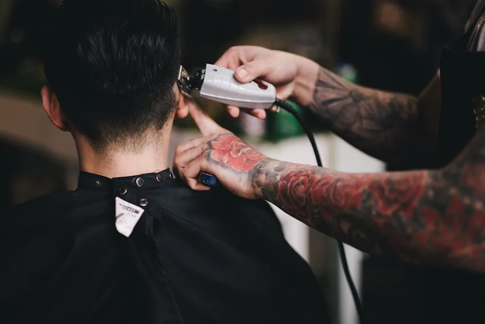 Der Barbier setzt die Haarschneidemaschine im Nacken an, der Kunde sitzt im schwarzen Umhang