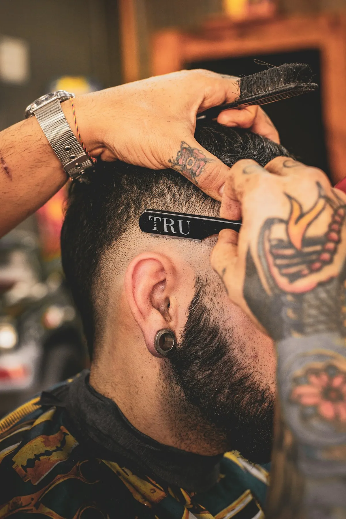 Nahaufnahme eines Skin Fades: der Barbier zieht mit dem Rasiermesser die Kante über dem Ohr nach
