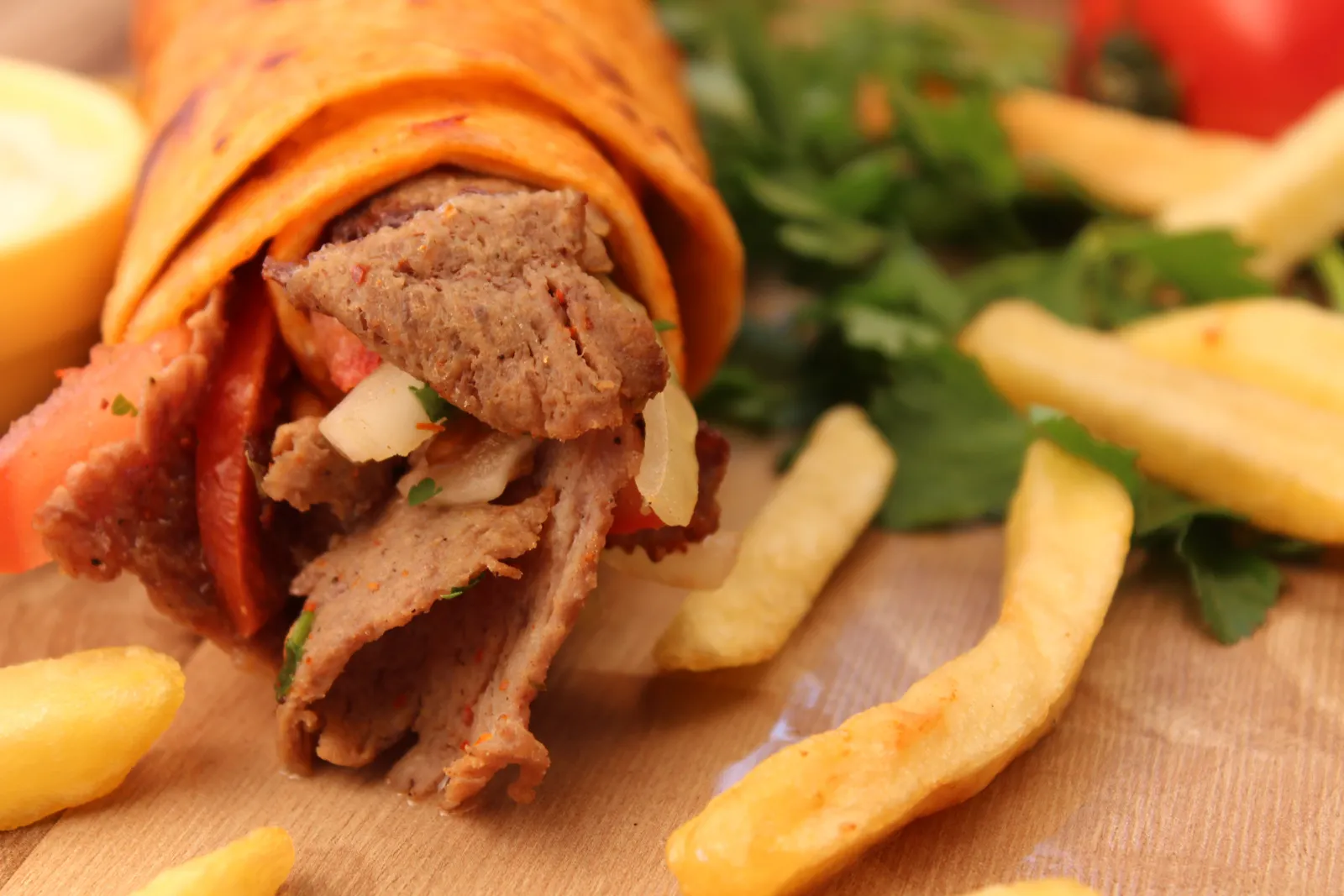 Aufgeschnittener Dürüm Kalb mit Fleisch vom Spieß, Tomate und Zwiebeln, daneben Pommes