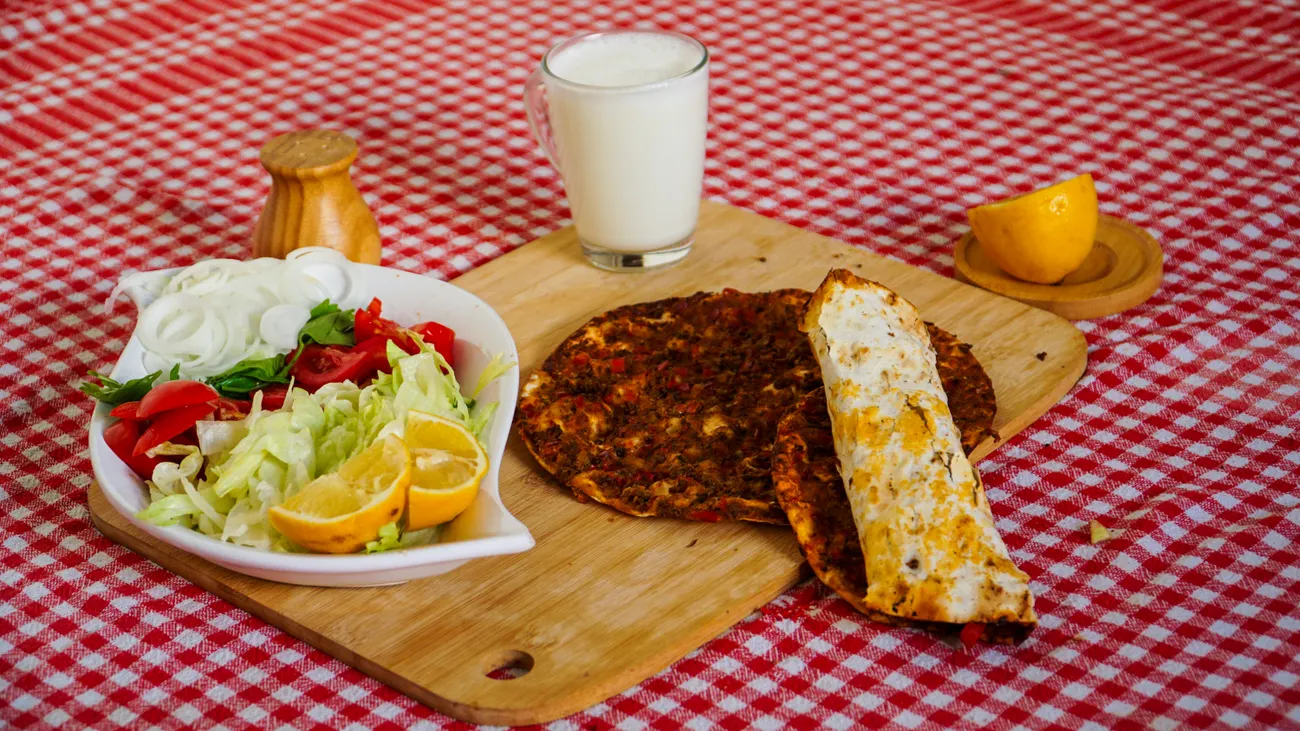 Gedeckter Tisch mit Lahmacun, frischem Salat und einem Glas Ayran auf rot kariertem Tuch