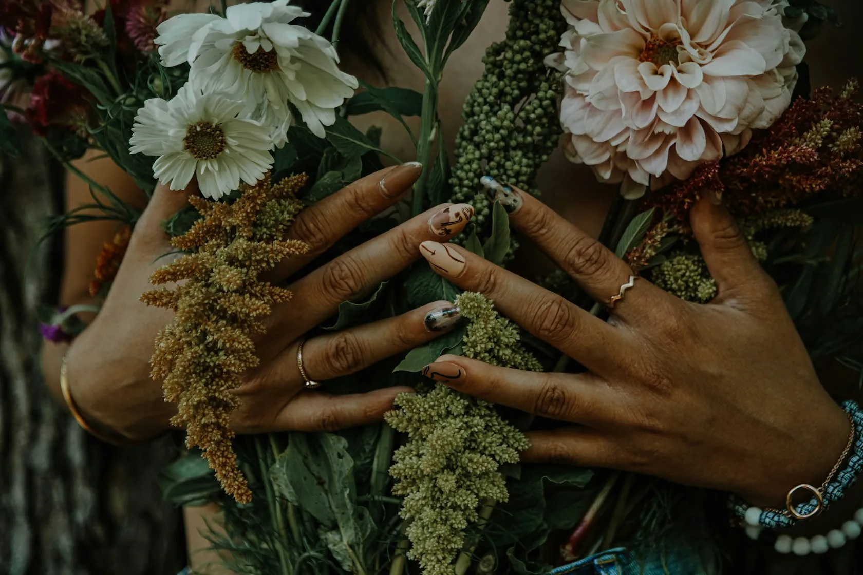 Zwei Hände mit Ringen halten einen Strauß Trockenblumen, die Nägel sind kurz und schlicht lackiert