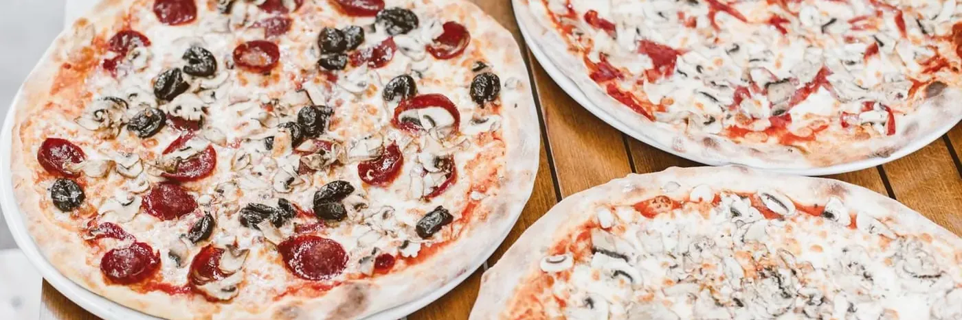 Drei dünn ausgebackene Pizzen mit Salami, Champignons und Oliven auf einem Holztisch