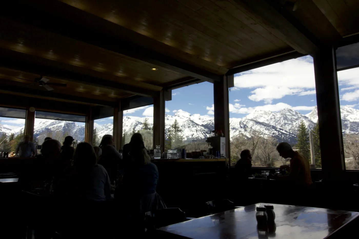 Dunkler Innenraum in Gegenlicht, Gäste als Silhouetten vor der verschneiten Bergkette.